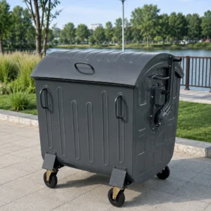 Contenedor de residuos de metal gris oscuro de cuatro ruedas con tapa curvada, instalado al aire libre a orillas de un lago