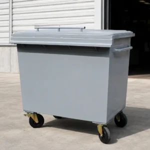 Metal four-wheel waste container with hinged lid outside an industrial facility